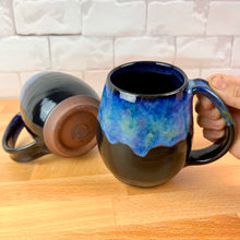 Load image into Gallery viewer, Aurora Borealis Mugs. each one is different. northwest style coffee mug thrown Red Stoneware, with large pulled handle. black glaze base with swirls of blue, turuoise, and hints of purple, reminiscent of the Aurora Borealis. this image shows the trimmed foot or bottom of the mug.