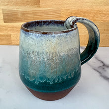 Load image into Gallery viewer, A handmade ceramic mug with a pulled handle, featuring a glaze that transitions from speckled white at the top to a deep teal over a deep red-brown stoneware clay. Forest Mist Mug