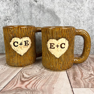 Large custom coffee mugs with lumberjack, woodgrain pattern impressed and carved in for texture you can feel. the mugs have a heart carved into them with initials, like lovers would carve into a tree