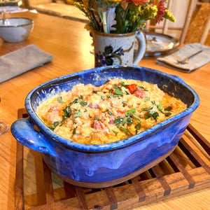 Casserole dish in cobalt Blue World glaze. shown with a spaghetti squash baked in it. wheel thrown and altered, with pulled handles added. made with stoneware clay.