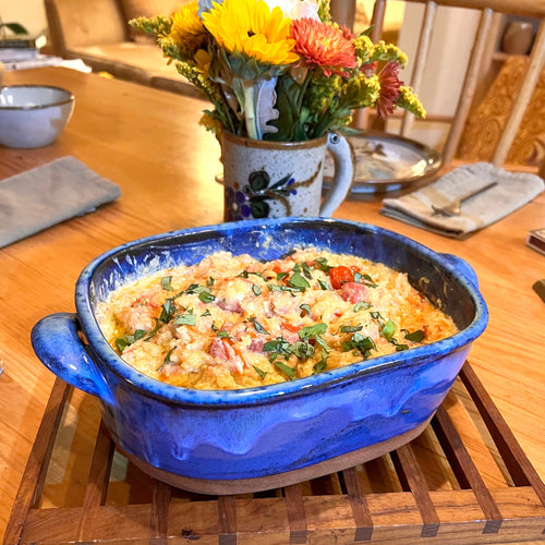 Casserole dish in cobalt Blue World glaze. shown with a spaghetti squash baked in it. wheel thrown and altered, with pulled handles added. made with stoneware clay.