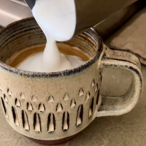 Pouring foamed milk into an espresso in awheelthrown carved mugs glazed in rustic white glaze. the carved facets show through the white glaze. these mugs are dishwasher safe too.