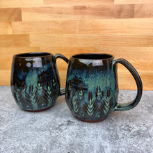 Load image into Gallery viewer, Two Beautiful, moss green glazed mugs. These are wheel thrown, and hand carved. the carvings allow the glaze to show through a bit at the edges, bringing variation to the glaze. This glaze has translucent areas and mottled, colorful areas.