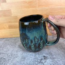 Load image into Gallery viewer, Beautiful, moss green glaze on a wheel thrown, hand carved northwest mug. the carvings allow the glaze to show through a bit at the edges, bringing variation to the glaze.