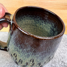 Load image into Gallery viewer, detail and inside of the Beautiful, caramel glaze on a wheel thrown, hand carved northwest mug. the carvings allow the glaze to show through a bit at the edges, bringing variation to the glaze. this glaze also shows the deep red clay color beneath it.