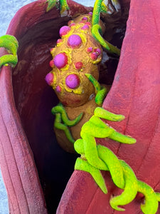 Close-up of a colorful, textured object with green tentacle-like structures inside a red container.