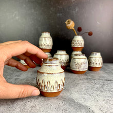 Load image into Gallery viewer, a collection of small bud vases , each one is hand carved with facets, with dried flowers in one of them. the vases are about 1.5-2 inches tall, wheelthrown in red stoneware, 