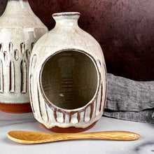 Load image into Gallery viewer, Salt Cellar, also known as a salt well or salt pig. shown here with matching Olive oil cruet. Wheel thrown and carved. comes with a bamboo spoon and a starter sea salt packet.. Thrown in a red stoneware clay, with a handled top, and carved by hand. the white glaze accentuates the carved pattern where the red clay shows through. Fern Street Pottery
