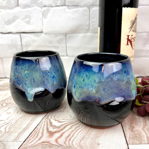 Stemless wine glasses. set of two wheel thrown pottery with finger divots for grip. Black glaze on the tumbler with bright blues and turquoise colors mixed similar to the Aurora Borealis as a glaze over stoneware clay