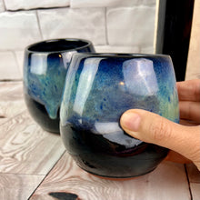 Load image into Gallery viewer, Stemless wine glasses. set of two wheel thrown pottery with finger divots for grip. Black glaze on the tumbler with bright blues and turquoise colors mixed similar to the Aurora Borealis as a glaze over stoneware clay