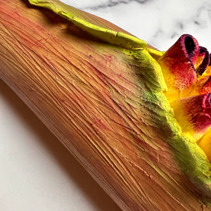 closeup image of a seedpod sculpture by meredith chernick of fern street pottery. the sculpture is made of porcelain and cold finished in bright colors with smooth hombre blends. this sculpture depicts a seedpod's husk with small protrusions emerging from within.