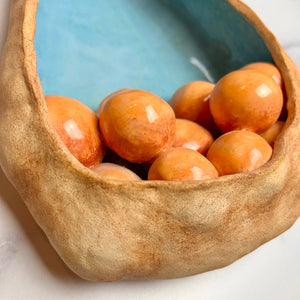 closeup, detail shot of See Pod inspired wall sculpture, stoneware husk like nest of seeds or eggs in light orange with a blue interior