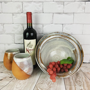 two pottery wine tumblers in speckled white, shown here with two matching serving bowls