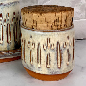Canister for beautiful display and storage. this canister is made from red stoneware clay, carved with a pattern and glazed in a speckled white glaze. the canister has a natural, rough cork lid. approximately 3.5 inches wide and 3.5 inches tall