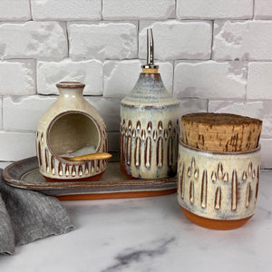 Canister for beautiful display and storage. this canister is made from red stoneware clay, carved with a pattern and glazed in a speckled white glaze. the canister has a natural, rough cork lid. approximately 3.5 inches wide and 3.5 inches tall. shown here with the olive oil cruet, salt cellar and tray (set sold separately)