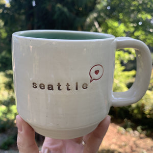 seattle "love" mug, wheelthrown with heart in speech bubble image and the word seattle inset. white exterior, glossy turquoise interior