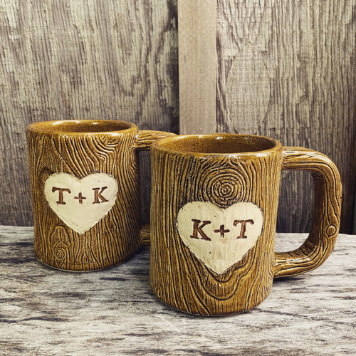 Large custom coffee mugs with lumberjack, woodgrain pattern impressed and carved in for texture you can feel. the mugs have a heart carved into them with initials, like lovers would carve into a tree